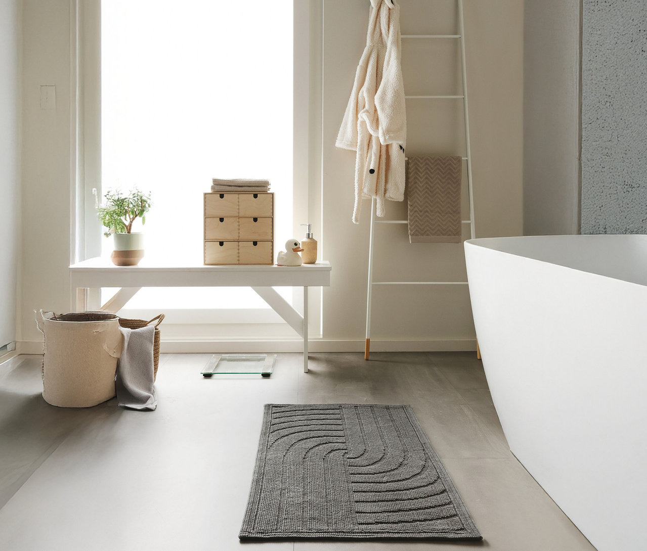 Ein anthrazitfarbener »Jojo« Badteppich von benuta mit Wellenmuster liegt im Badezimmer.