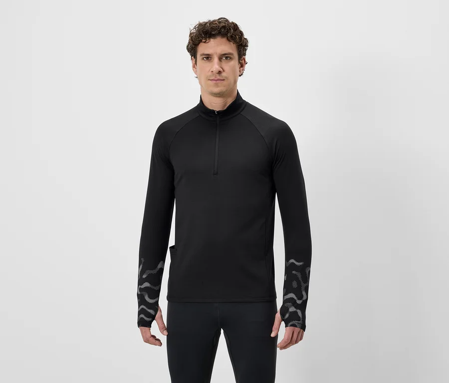 Ein Mann mit lockigem Haar trägt ein schwarzes, langärmeliges Shirt mit Reißverschluss und Leggings vor einem weißen Hintergrund.