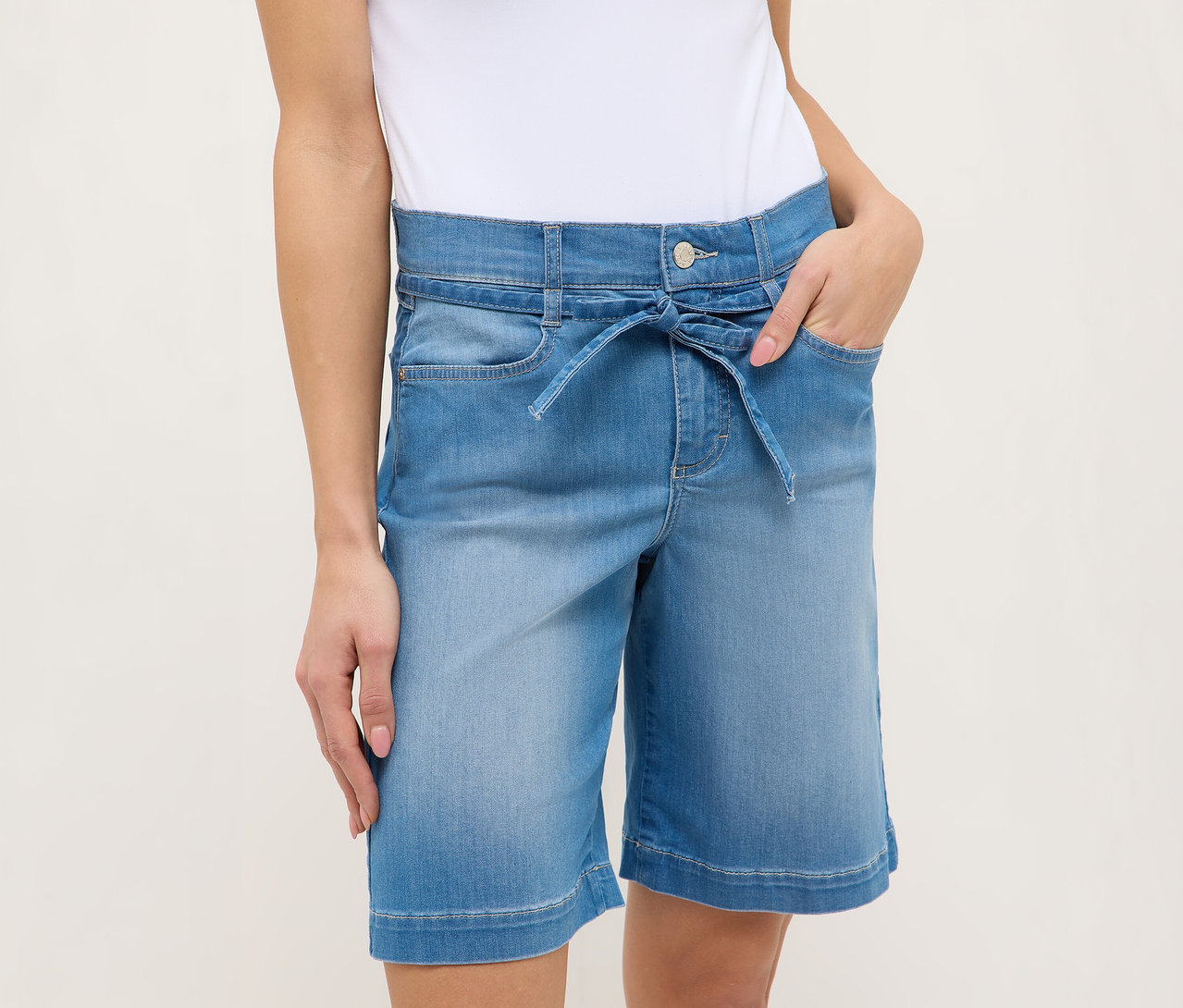 Frau mit Angels Denim »Lia City« Shorts, hellblau, mit Bindegürtel und Händen in den Taschen.