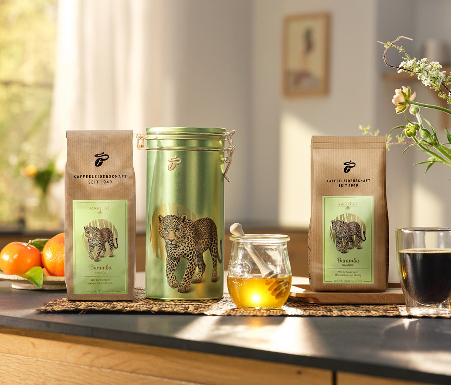Auf einer Küchentheke stehen eine Kaffeedose und zwei Packungen »Buramba Rwanda« inkl. Kaffeedose neben einer Tasse Kaffee und Honig.