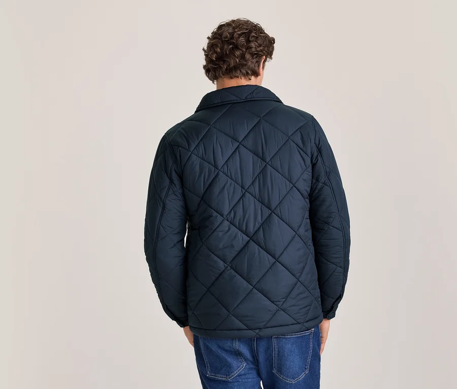 Mann von hinten in einer dunkelblauen Steppjacke und blauen Jeans, mit lockigem braunem Haar.