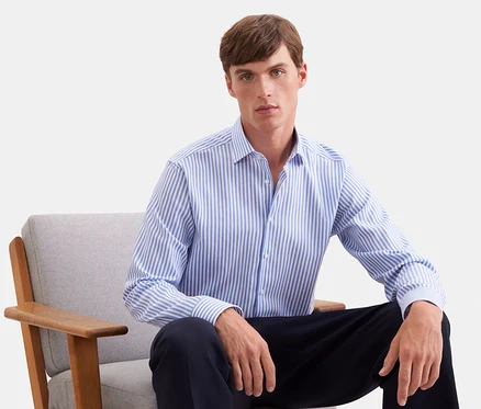 Mann sitzt in einem grauen Sessel, trägt ein blau-weiß gestreiftes Langarmhemd und eine dunkle Hose.