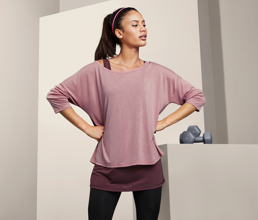 Frau posiert mit Händen in den Hüften in einem 2-in-1-Sportshirt.