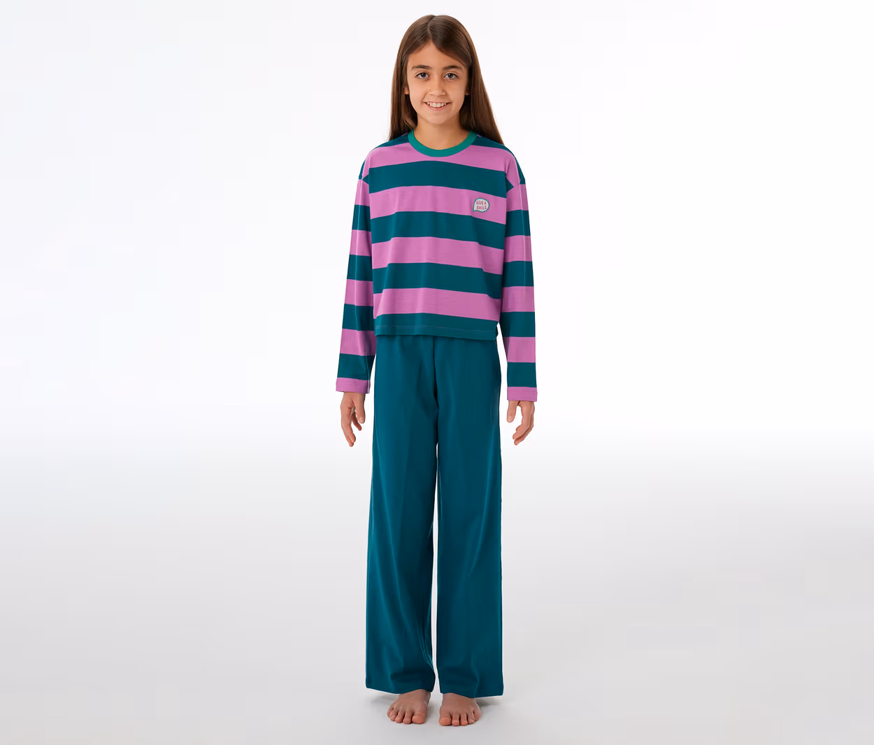 Ein junges Mädchen steht lächelnd barfuß in einem gestreiften SCHIESSER Kinder-Pyjama in Lila und Türkis mit passender Hose.