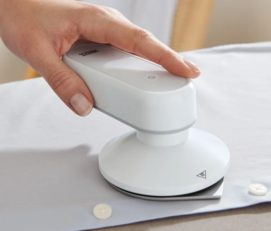 Eine Hand bügelt ein weisses Hemd mit einem Princess-Reisebügeleisen mit Powerbank.