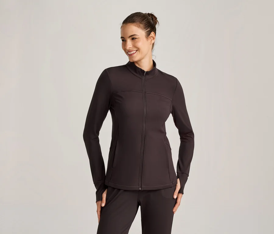 Eine lächelnde Frau trägt eine dunkelbraune Sportjacke mit Reißverschluss und passender Hose.