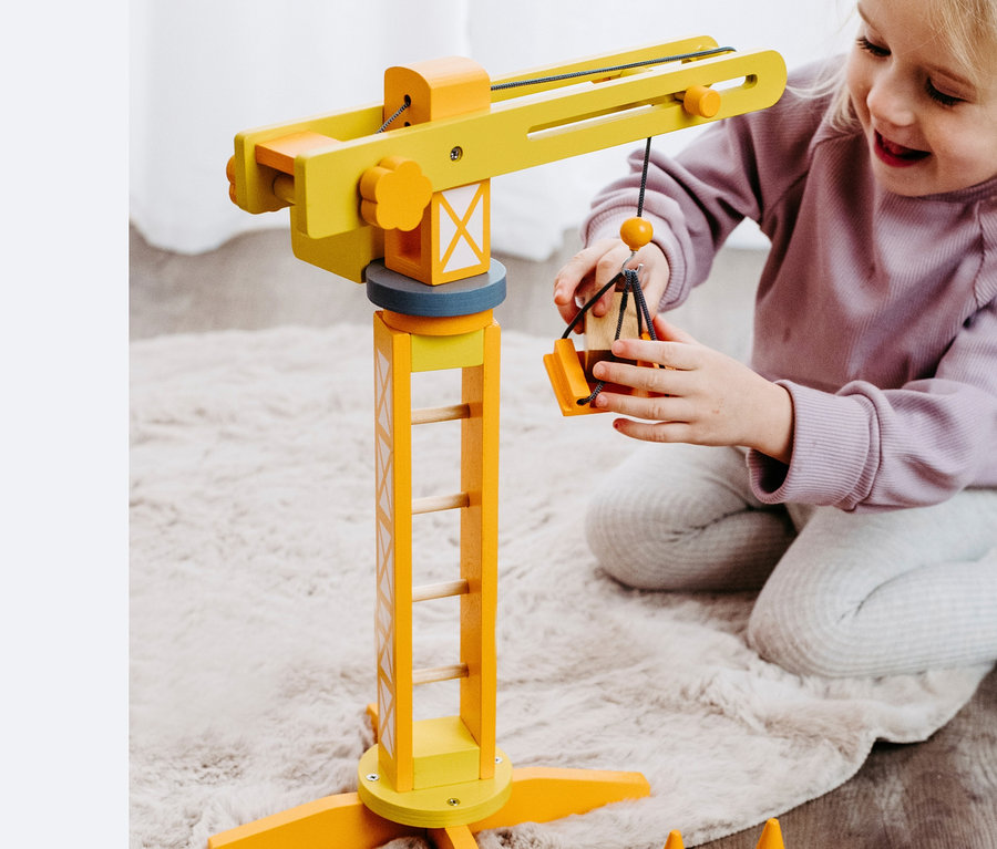 Mädchen spielt mit einem gelben small foot Baukran mit Baustellenzubehör aus Holz.