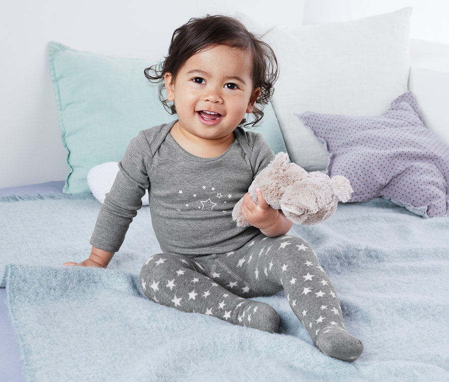 Ein Baby sitzt auf einem Bett und trägt eine graue Thermostrumpfhose mit Sternen, 2 Stück.