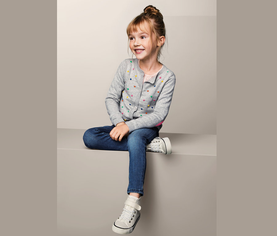 Lächelndes Mädchen sitzt und trägt eine Strickjacke, Jeans und Turnschuhe.
