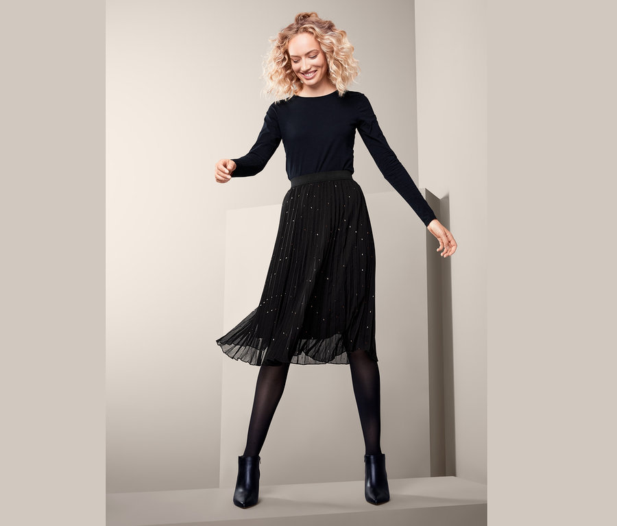 Frau trägt einen Plisseerock, eine schwarze Strumpfhose, schwarze Stiefel und ein schwarzes Langarmshirt.