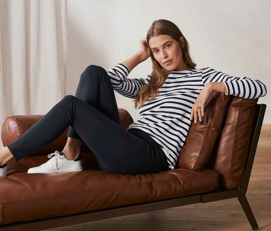 Frau sitzt auf Ledersessel, trägt dunkelblaue Basic-Leggings aus Heavy-Jersey.