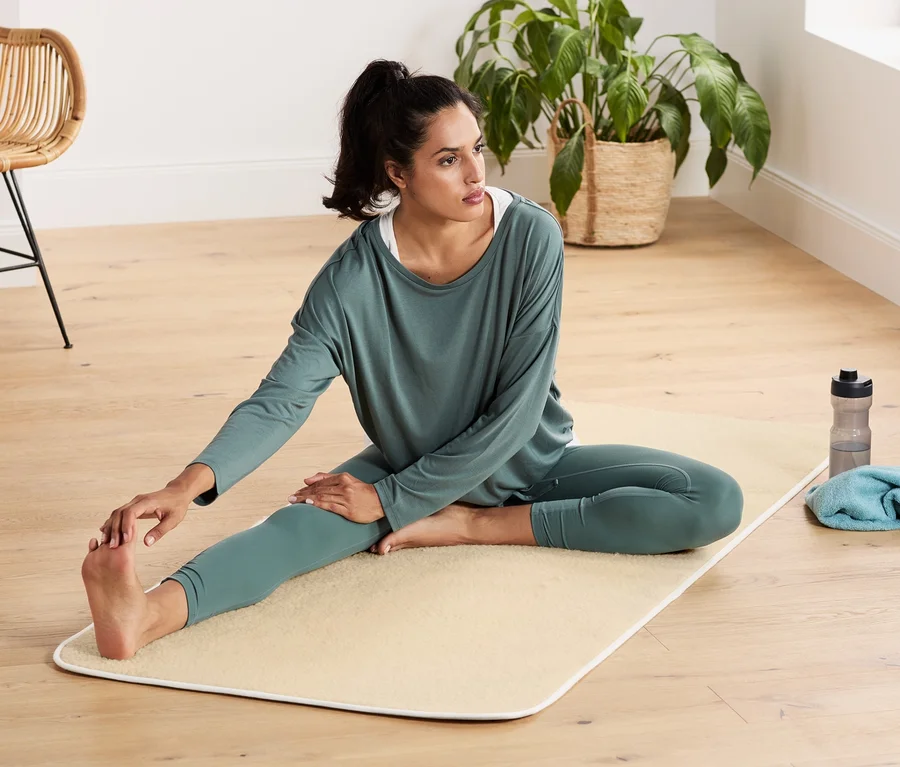 Frau dehnt sich auf einer Schurwoll-Yogamatte.