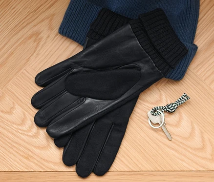 Auf einem Holzboden liegen eine blaue Strickmütze, Lederhandschuhe und ein Schlüssel.