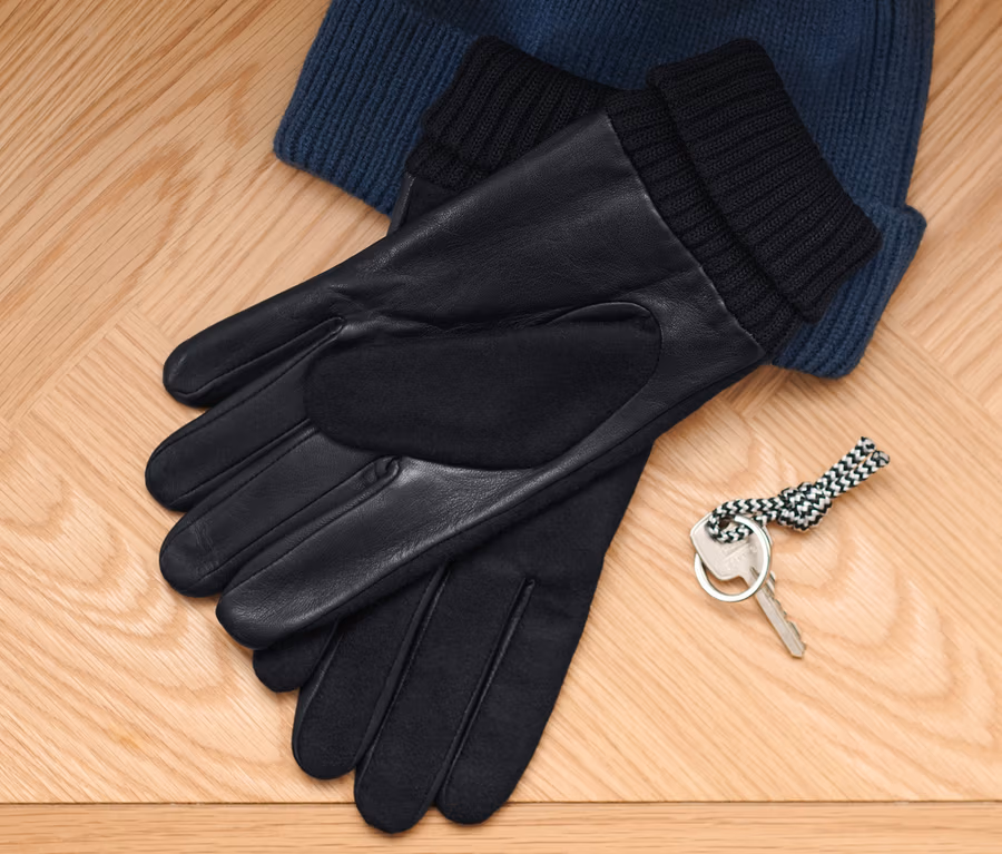 Auf einem Holzboden liegen eine blaue Strickmütze, Lederhandschuhe und ein Schlüssel.