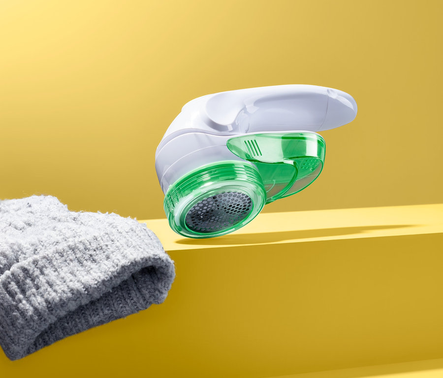 Ein Fusselrasierer mit schwenkbarem Kopf liegt neben einer grauen Strickmütze auf gelbem Hintergrund.