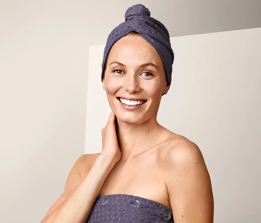 Frau lächelt mit Turban-Handtuch auf dem Kopf.
