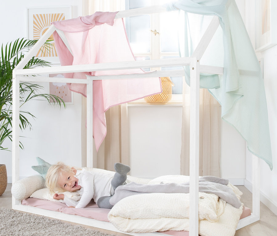 Ein Kind liegt in einem weißen roba Hausbett, ca. 70 x 140 cm, mit rosa und blauen Stoffen.