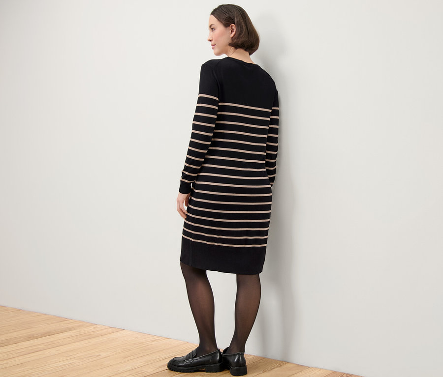 Frau steht seitlich und trägt ein gestreiftes Feinstrickkleid.