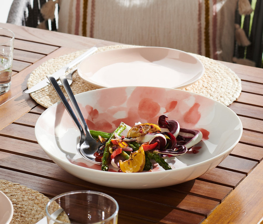 Auf einem Holztisch steht eine Porzellan-Schale mit Salat.