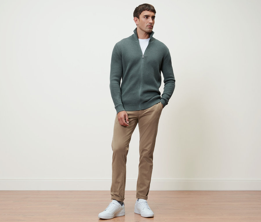Mann steht und trägt eine Strickjacke in Salbei und eine Chino in Sandfarben.