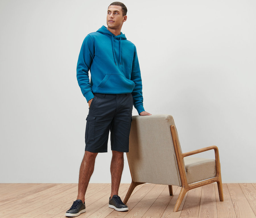 Mann posiert in blauem Hoodie und navy Cargo-Shorts.