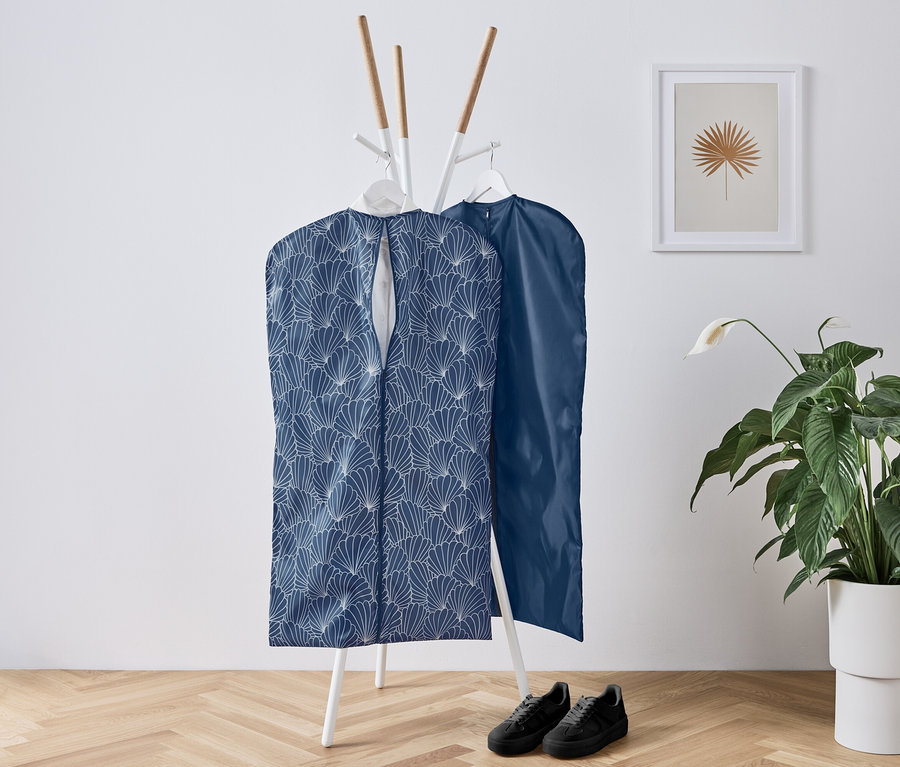 Zwei Kleiderschutzhüllen hängen an einer weißen Garderobe, darunter stehen schwarze Schuhe, daneben eine Blume.