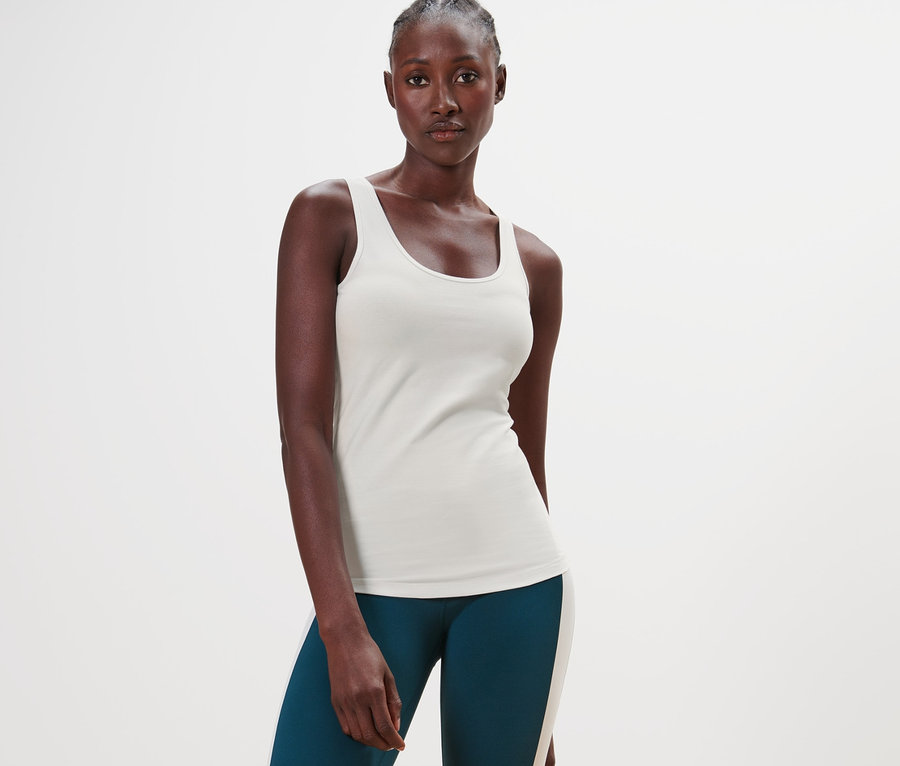 Eine dunkelhäutige Frau steht und trägt ein offwhite Top und grüne Leggings.