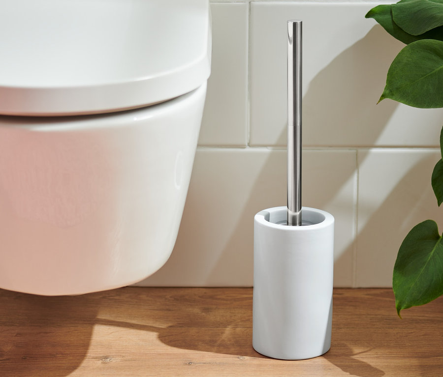 Eine WC-Schüssel und eine weiße WC-Bürste stehen auf einem Holzboden neben einem rosa Teppich.