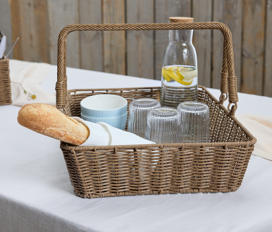 Ein Korbtablett mit Baguette, Gläsern und einer Karaffe mit Zitrone.