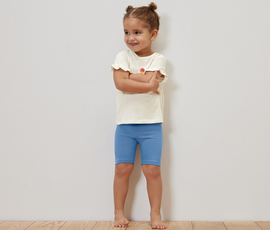 Ein Mädchen steht mit verschränkten Armen und trägt blaue Kinder-Radler-Leggings.