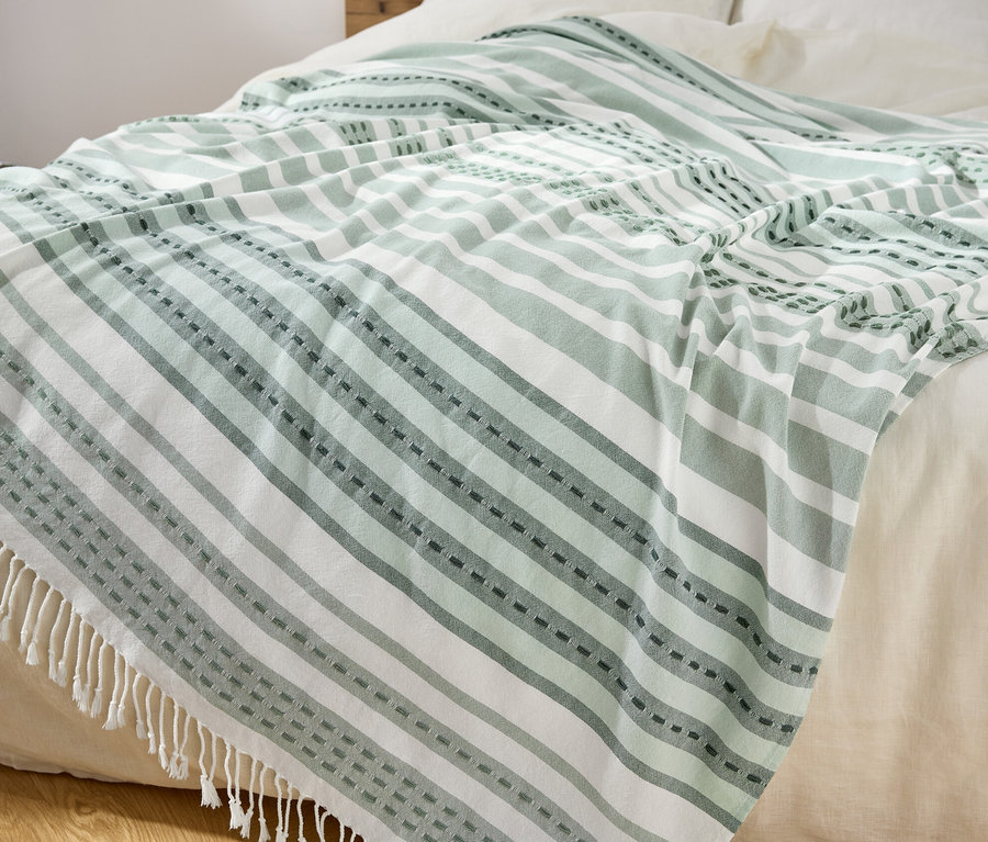 Auf einem Bett liegt ein grün und weiß gestreifter Plaid mit Fransen.