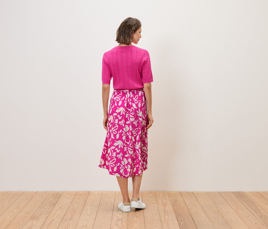 Frau mit dem Rücken zur Kamera trägt ein rosa Top und einen Rock mit Blumendruck.