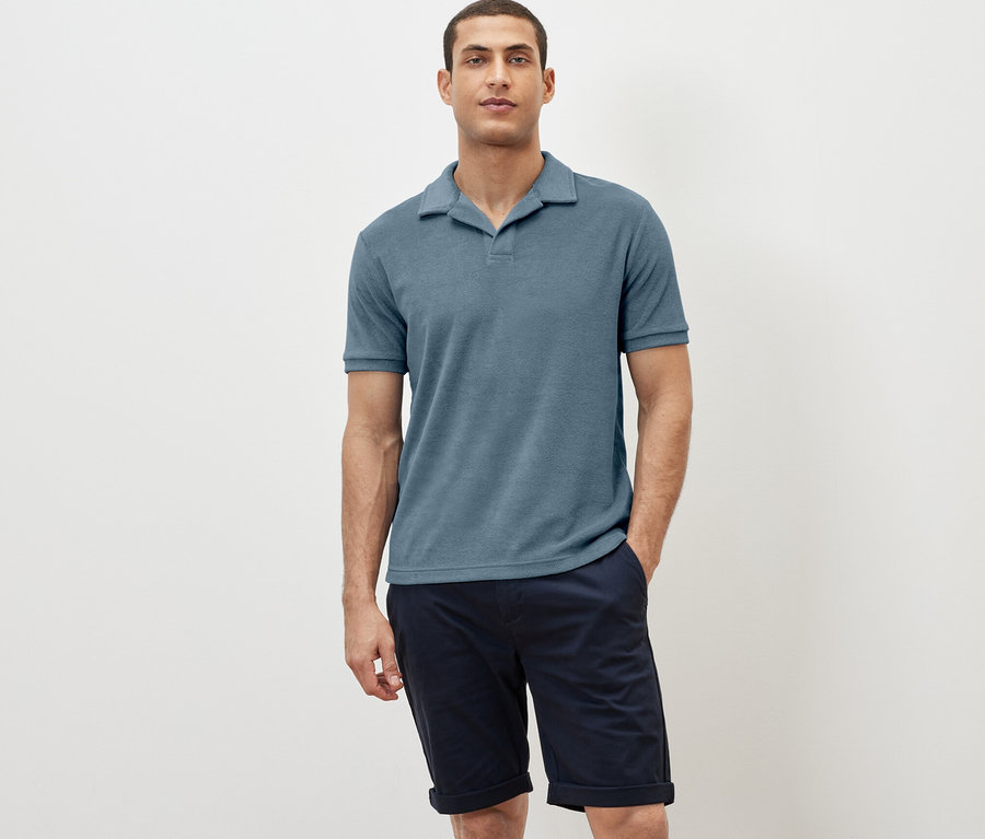 Mann posiert in einem blaugrauen Frottee-Poloshirt und dunkelblauen Shorts.