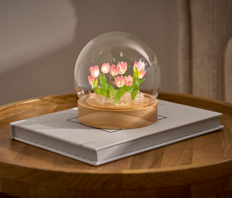 LED-DIY-Bastel-Set mit Tulpen in einer Glaskuppel auf einem Buch auf einem runden Tisch.