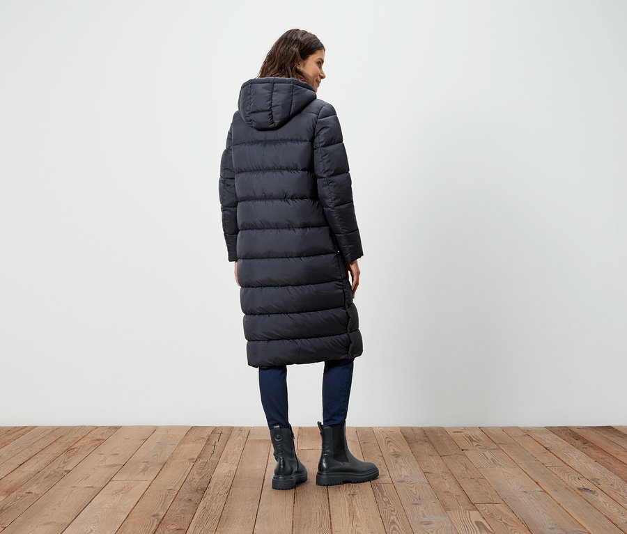 Frau von hinten trägt einen langen schwarzen Daunenmantel, Jeans und Stiefel.