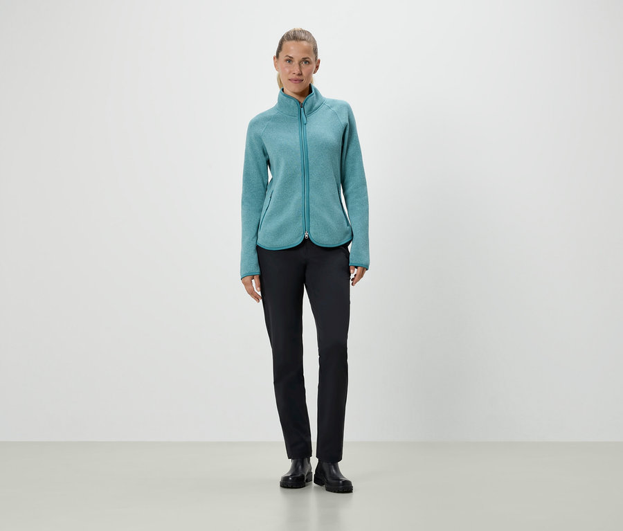 Frau steht in türkiser Fleecejacke und schwarzen Hosen.