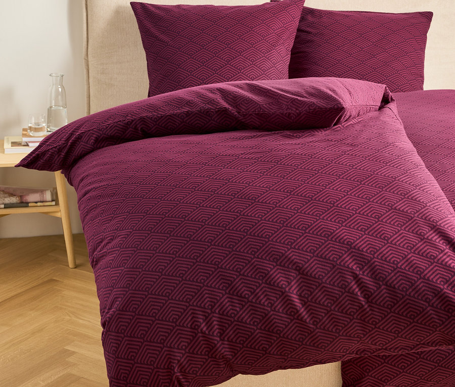 Burgunderfarbene Bettwäsche mit geometrischem Muster auf einem Bett.