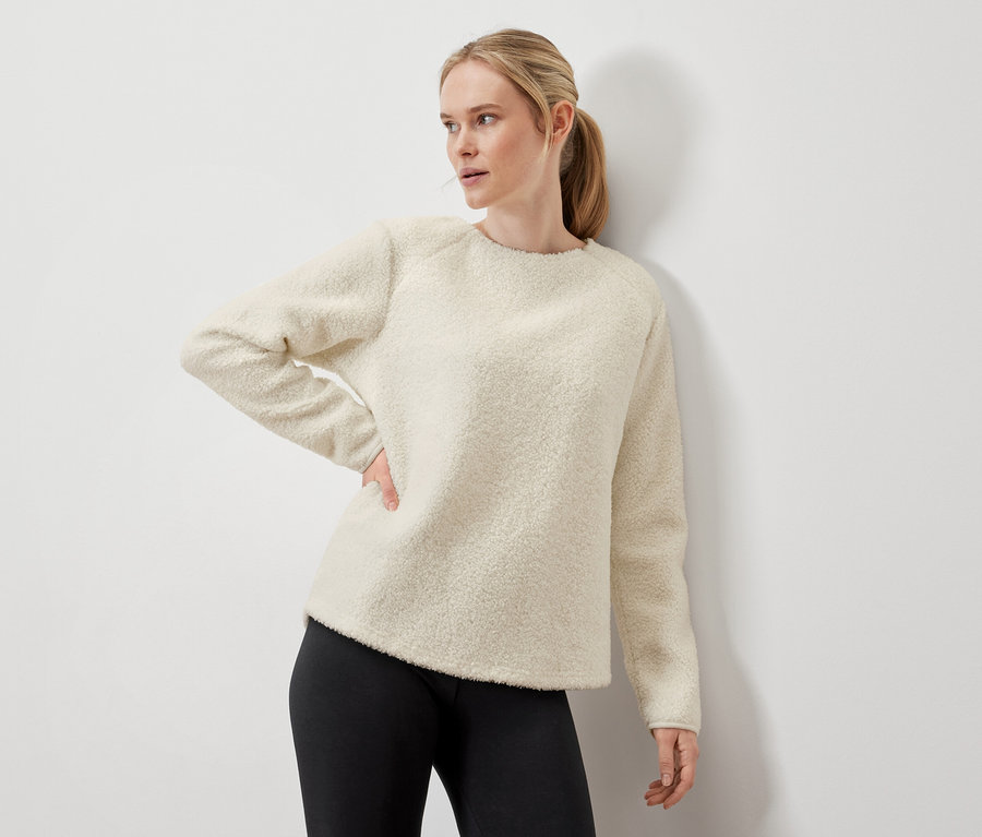 Frau posiert in cremefarbenem Pullover und schwarzen Leggings.