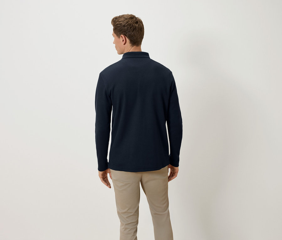 Ein Mann mit dem Rücken zur Kamera trägt ein dunkelblaues Langarm-Poloshirt und beige Hosen.