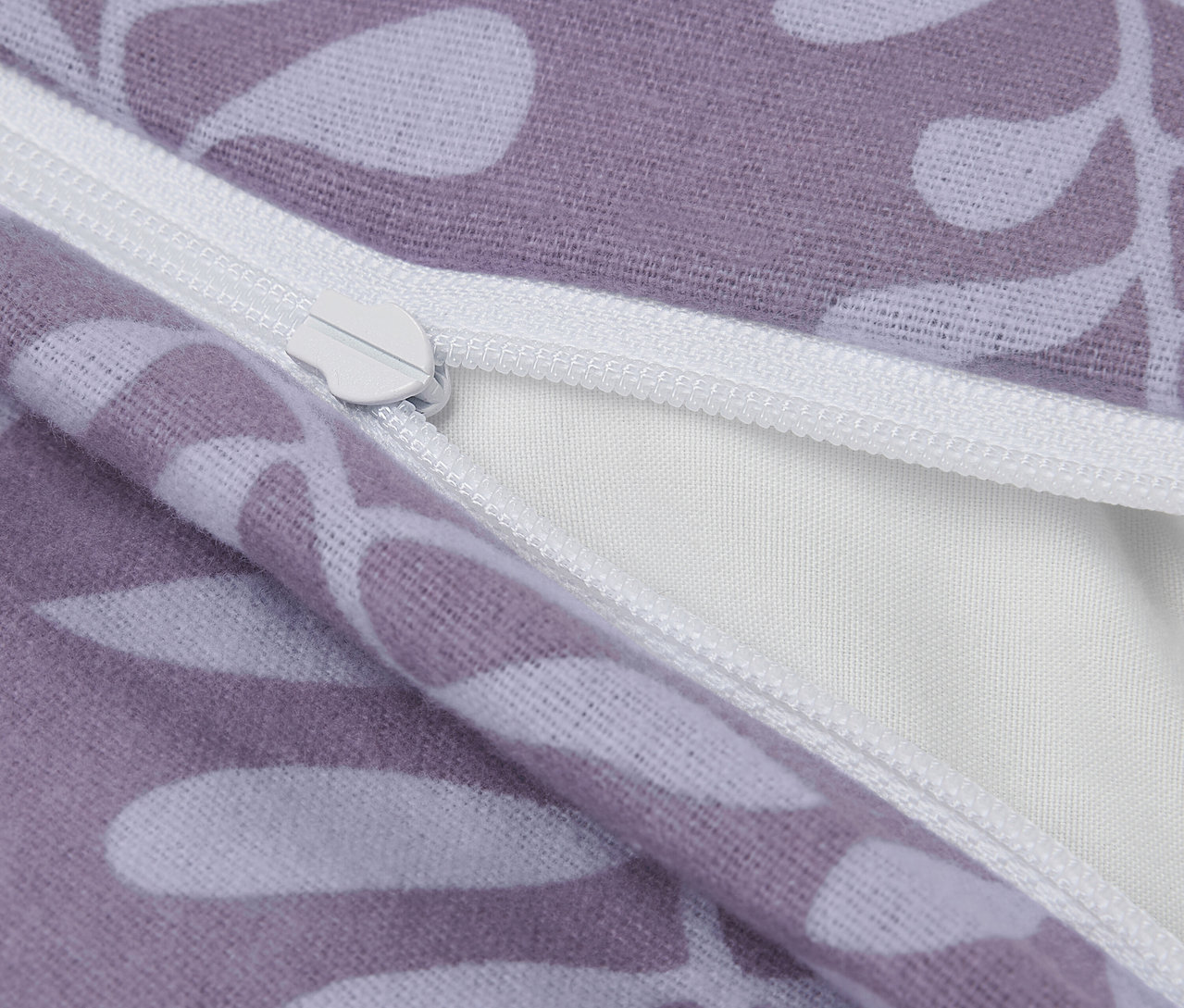 Detailaufnahme eines lila Kissenbezugs mit weißen Blättern und Reißverschluss.