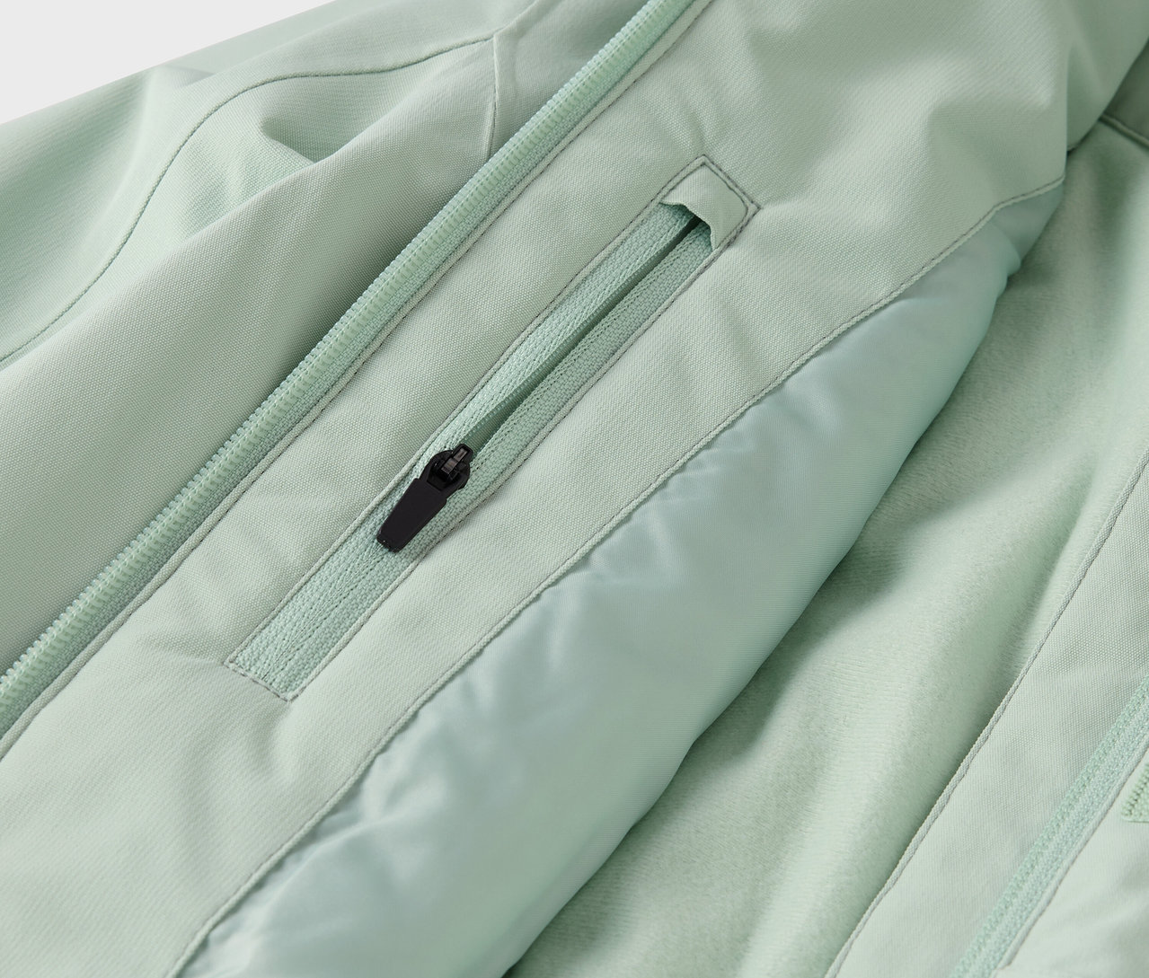Detailaufnahme einer hellgrünen Jacke mit Reißverschlusstasche und Reißverschluss in der Mitte.