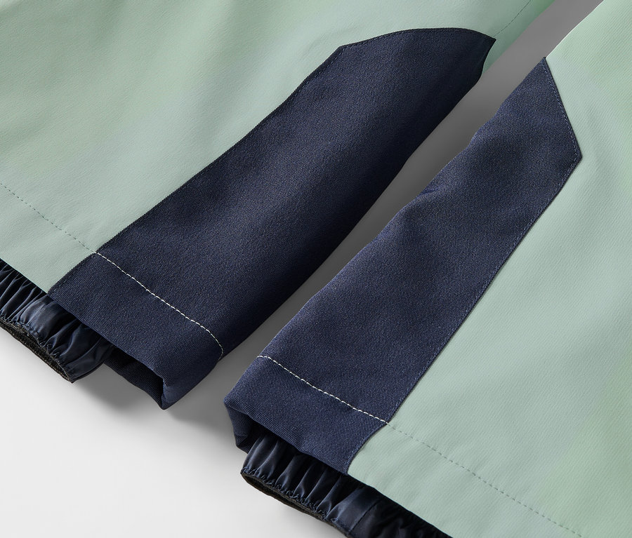 Detailaufnahme einer hellgrünen Jacke mit dunkelblauen Ärmeln und elastischen Bündchen.