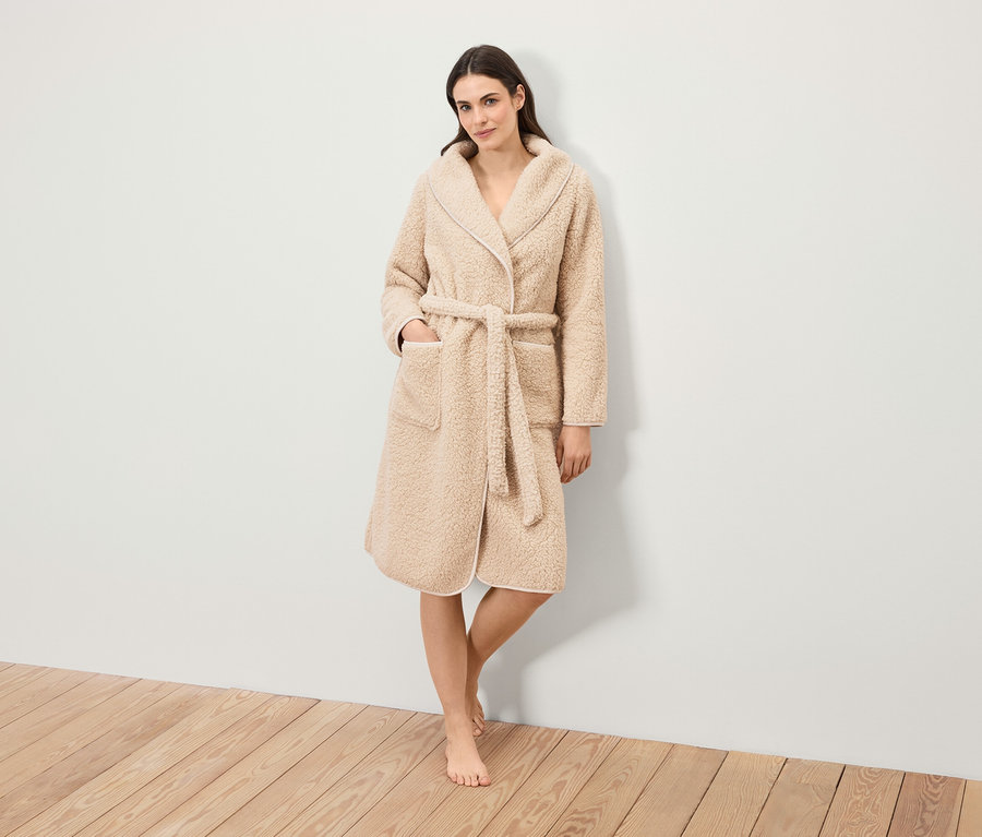 Eine Frau steht und trägt einen flauschigen Bademantel mit Gürtel.
