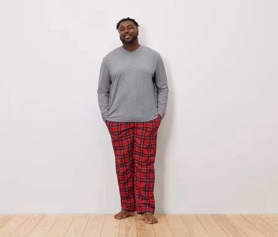 Ein Afroamerikaner steht mit den Händen in den Hosentaschen und trägt ein graues Langarmshirt und eine rot karierte Pyjamahose.