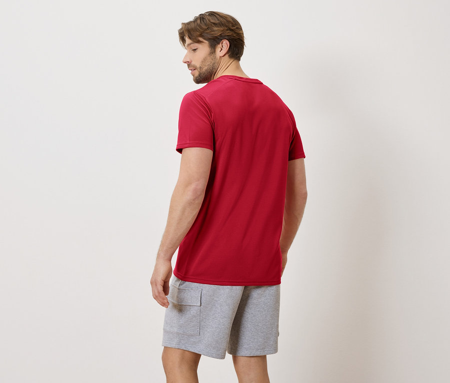 Mann von hinten in rotem T-Shirt und grauen Shorts vor neutralem Hintergrund.
