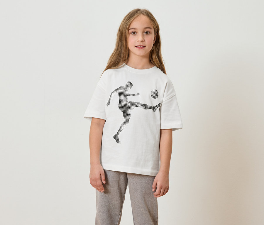 Mädchen mit langem Haar trägt ein weißes T-Shirt mit einem Fußballspieler-Aufdruck und graue Jogginghose.