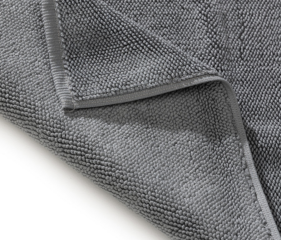 Nahaufnahme eines grauen Badvorlegers mit gefalteter Ecke.