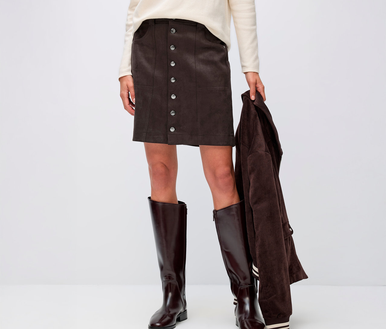 Frau trägt einen Street One Veloursrock, ein cremefarbenes Oberteil und braune Stiefel.