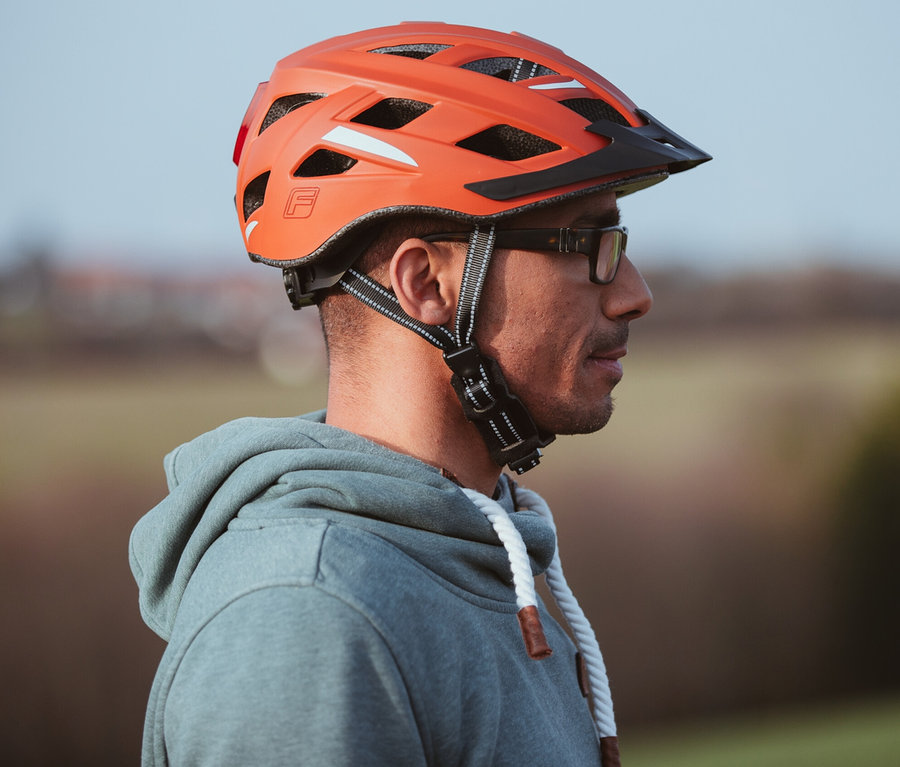 Ein Mann trägt einen orangefarbenen FISCHER Fahrradhelm Urban PLUS Miami.