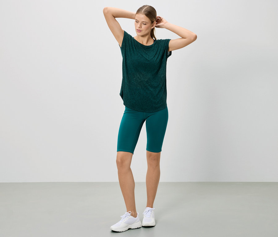 Frau posiert in einem dunkelgrünen T-Shirt und Shorts, dazu weiße Turnschuhe.